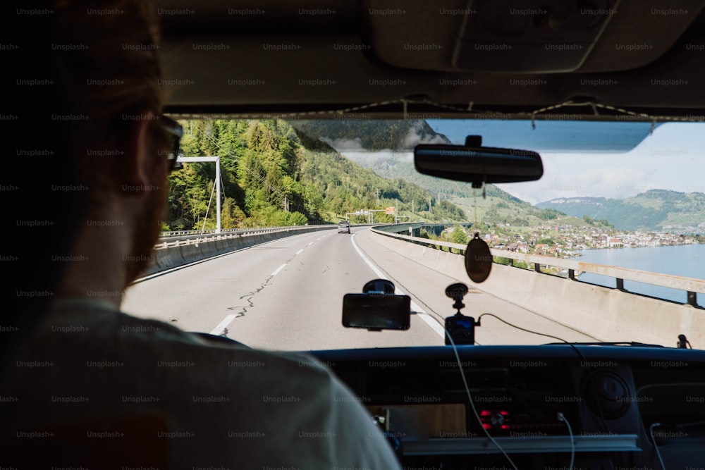 a man driving a car down a highway next to a lake