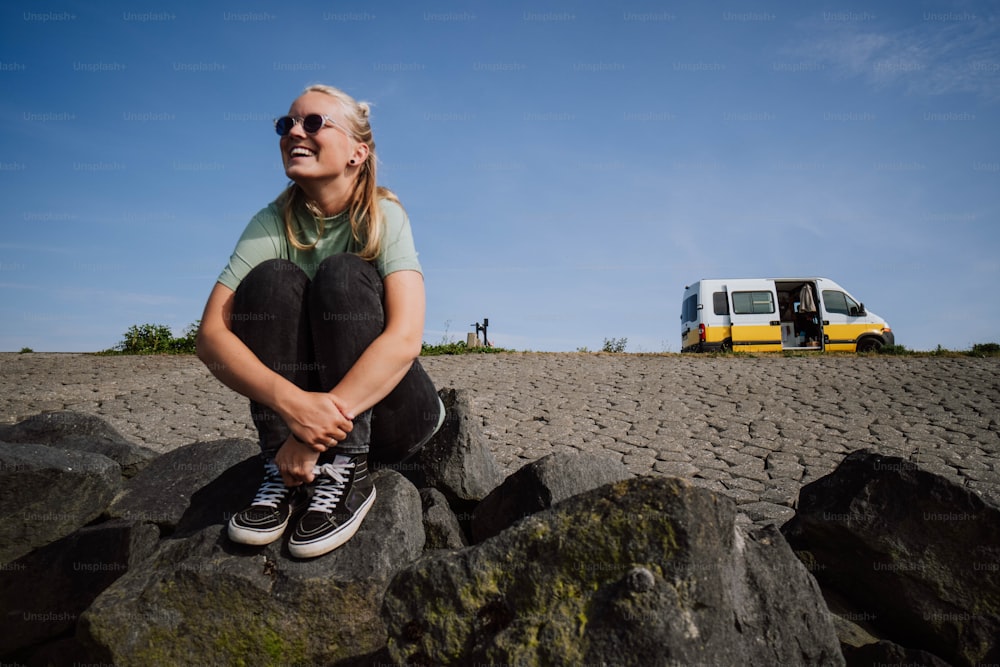 a woman sitting on a rock with a van in the background
