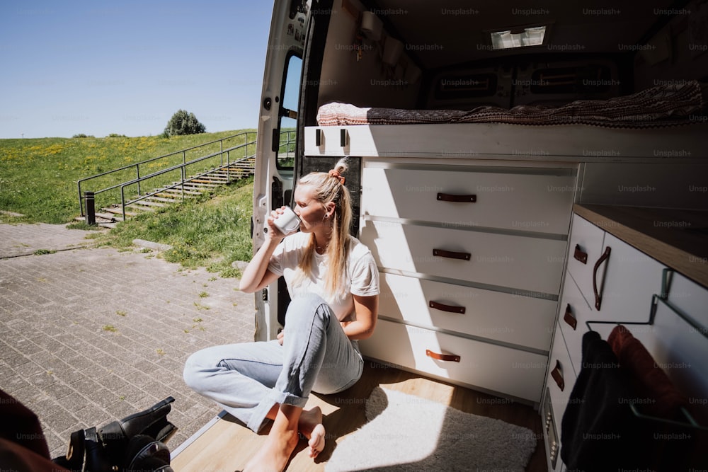 a woman sitting in the back of a truck drinking from a bottle