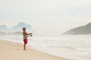 um homem de pé em uma praia segurando uma vara de pesca