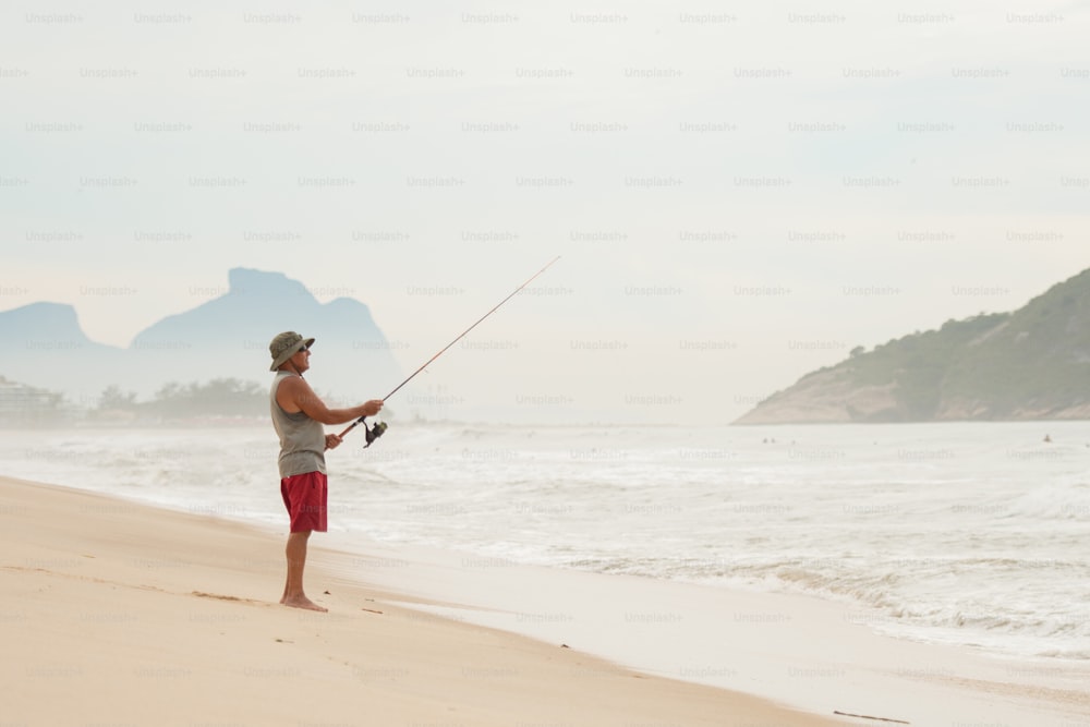 Un uomo in piedi su una spiaggia che tiene una canna da pesca