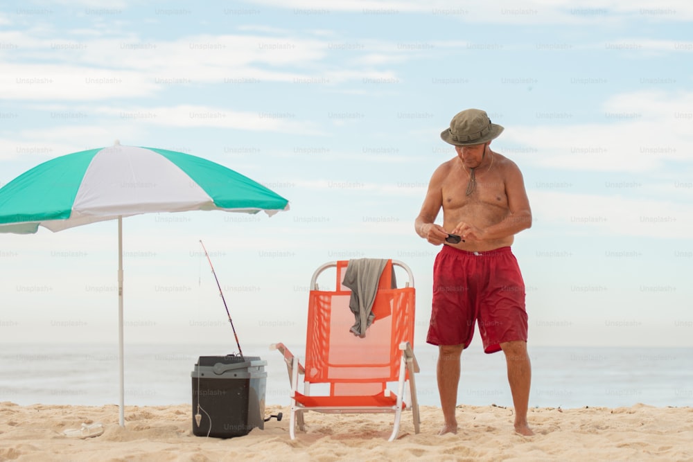 Un hombre parado en una playa junto a una silla y una sombrilla