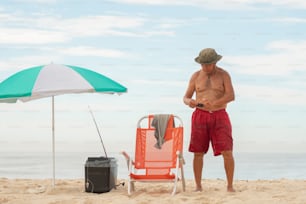의자와 우산 옆에 해변에 서있는 남자