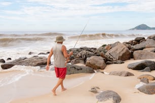 a man walking along a beach holding a fishing pole