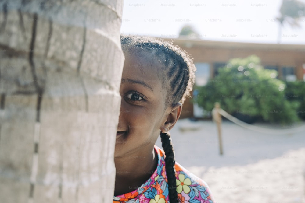 a young girl is peeking out from behind a tree