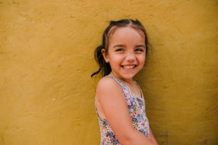 a little girl standing in front of a yellow wall
