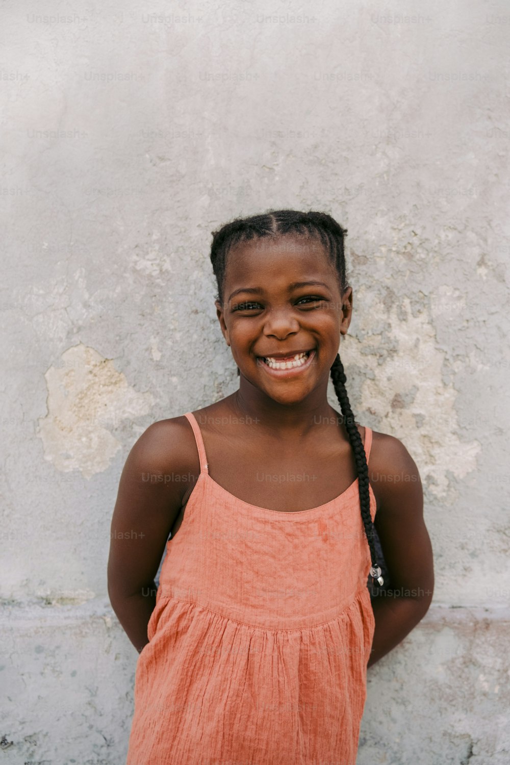 uma jovem sorridente com tranças em pé na frente de uma parede