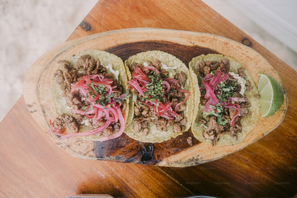 three tacos on a wooden platter on a table