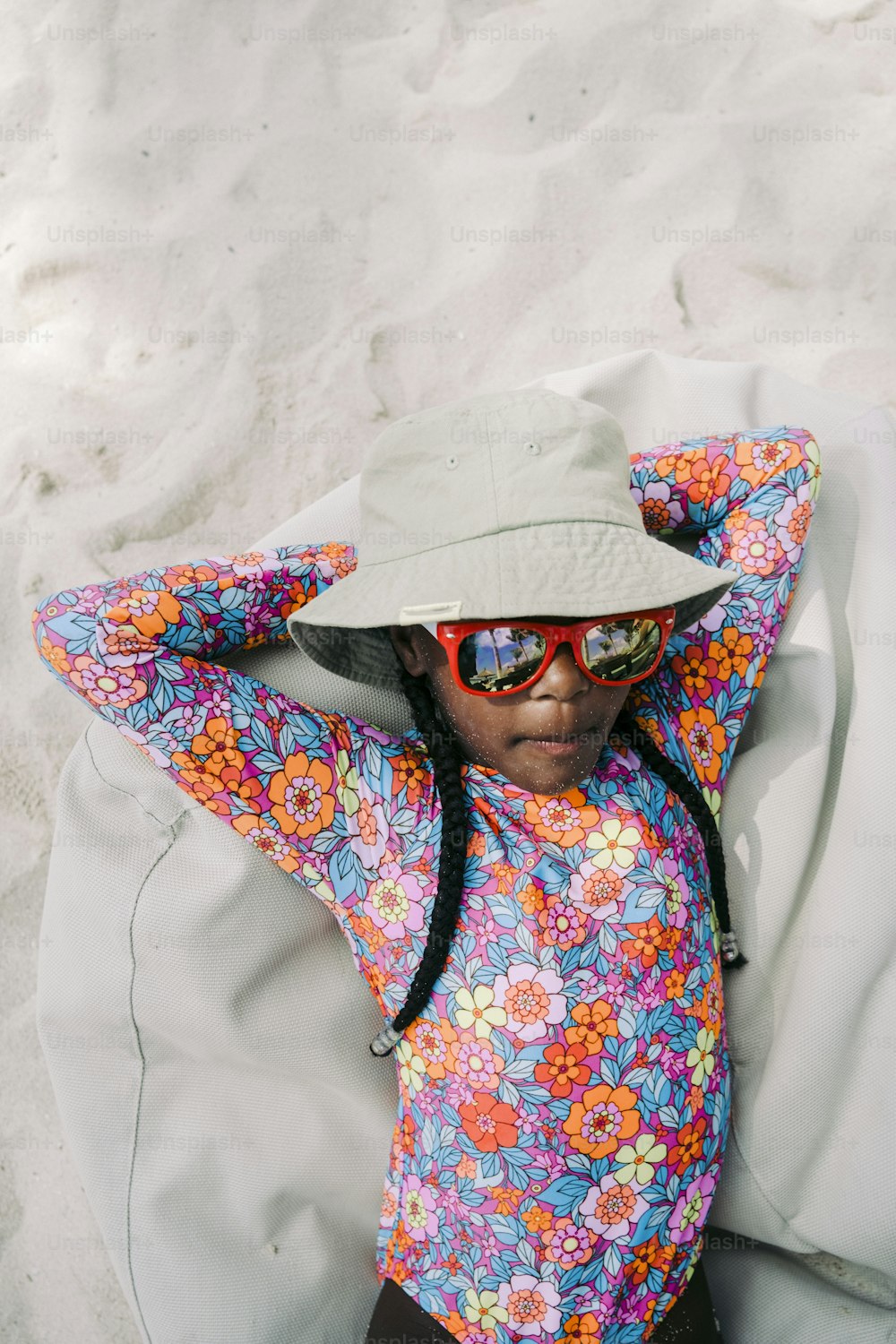 a little girl laying on a bean bag chair wearing a hat and sunglasses
