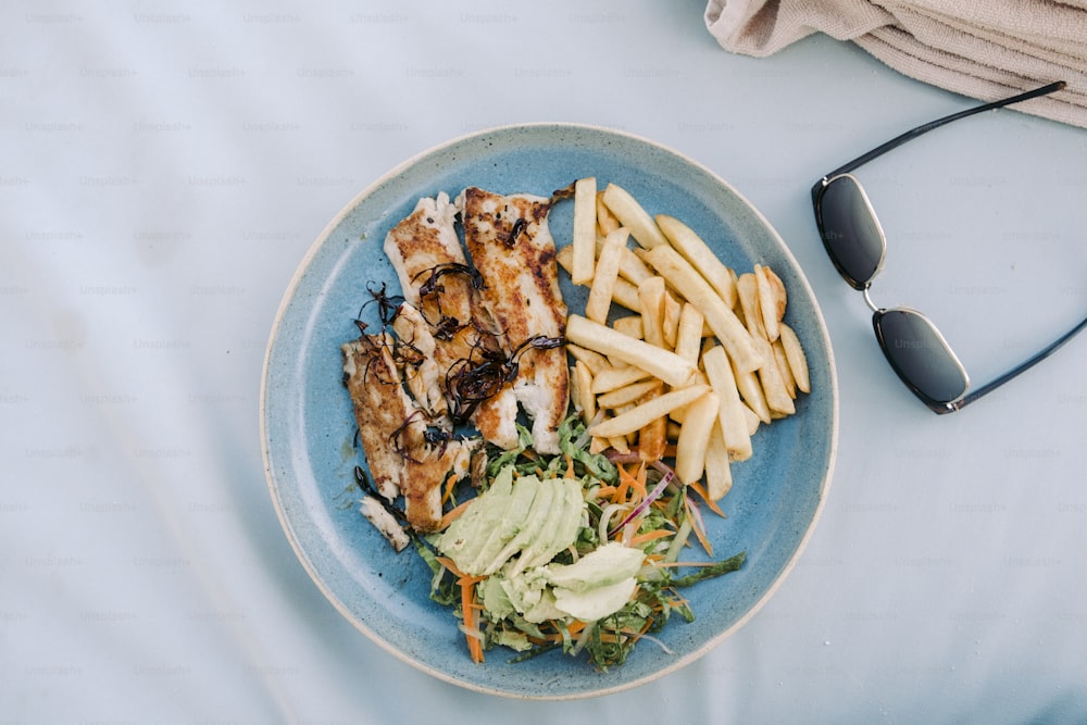 a blue plate topped with chicken, french fries and avocado