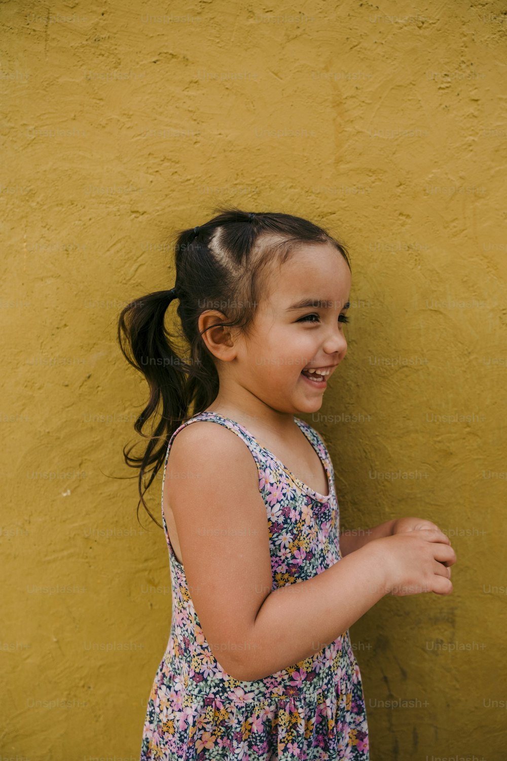 uma menina em pé na frente de uma parede amarela
