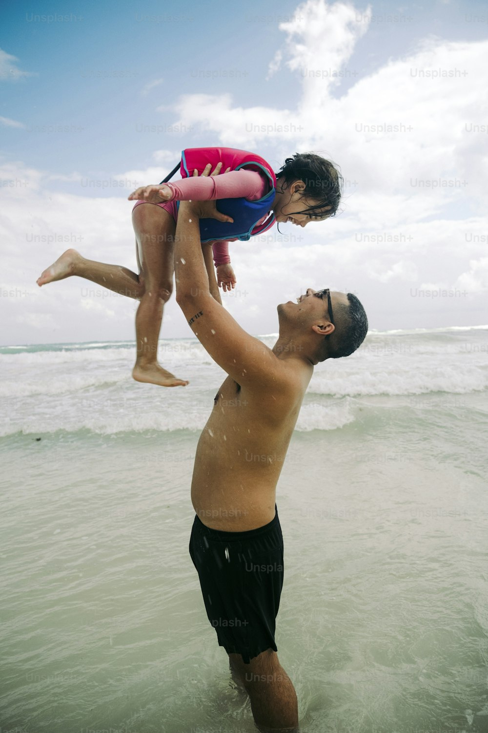 a man holding a little girl on his shoulders in the ocean