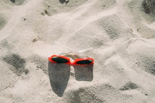 a pair of red sunglasses laying in the sand
