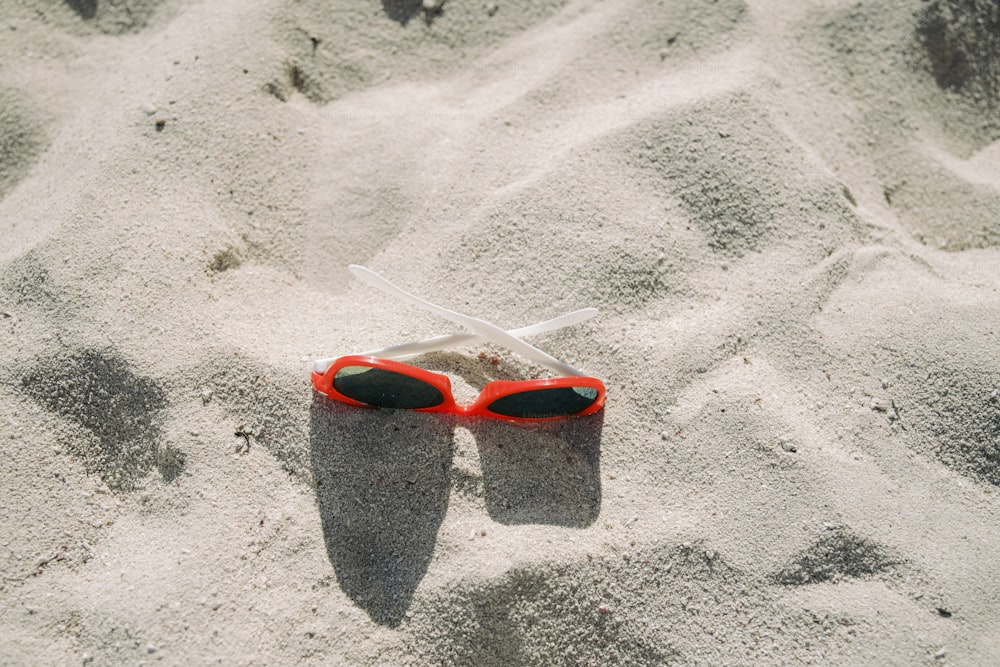 Un par de gafas de sol rojas tiradas en la arena