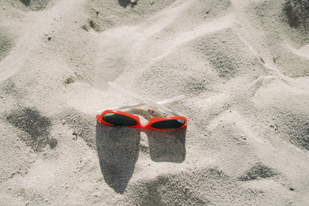 a pair of red sunglasses laying in the sand