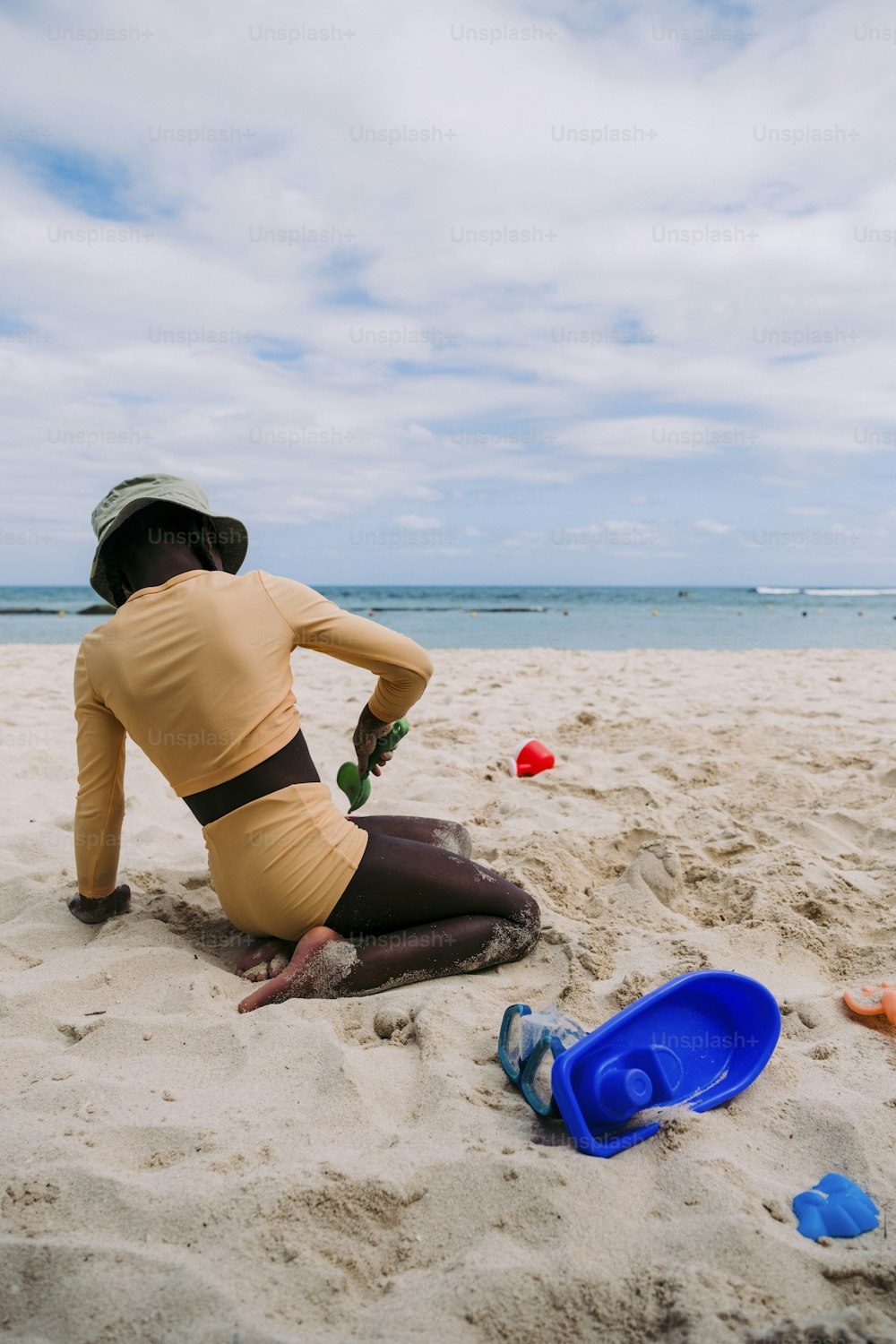 uma mulher sentada em uma praia ao lado de um frisbee azul