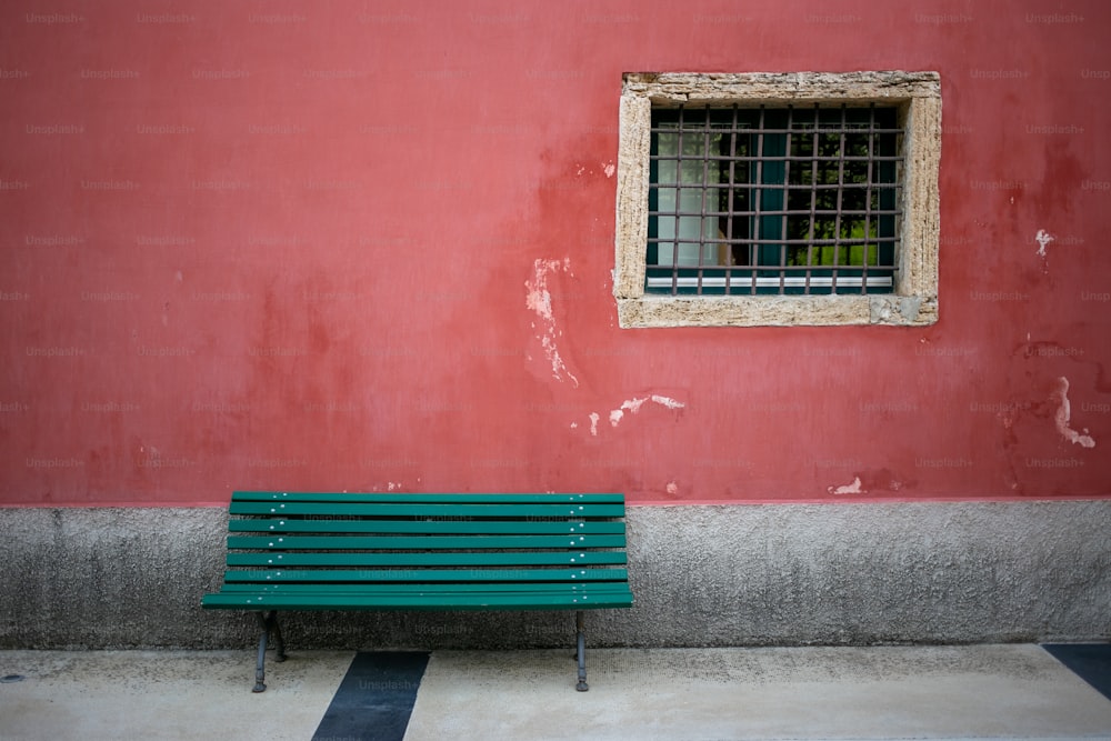 a green bench sitting in front of a red wall