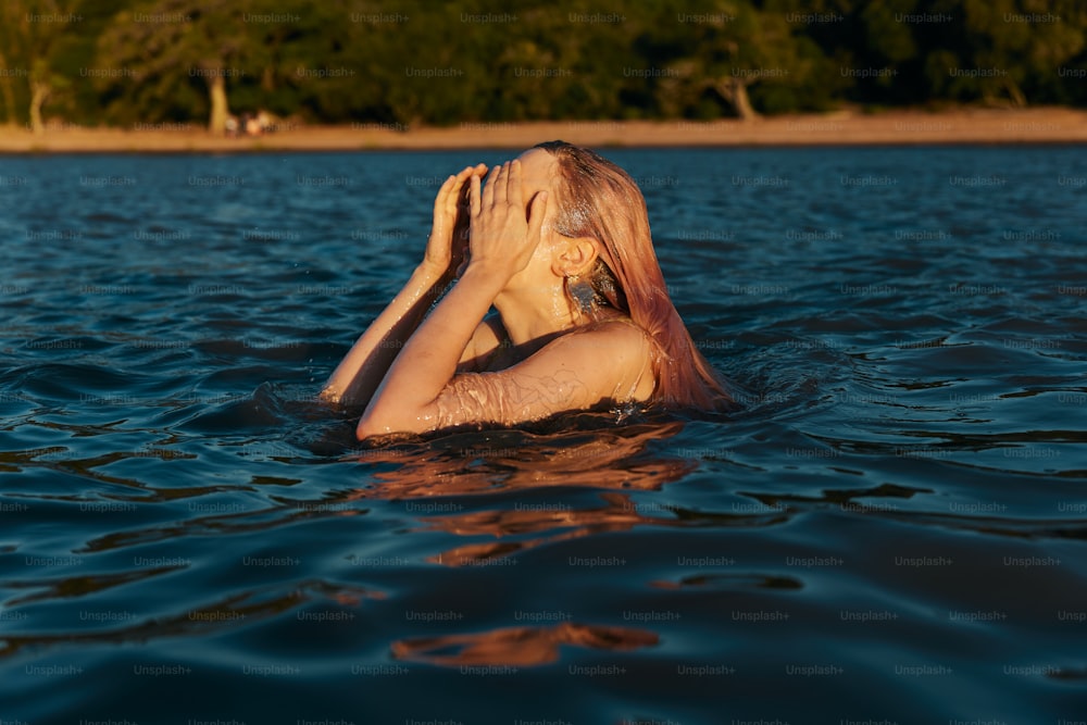 uma mulher na água cobrindo o rosto com as mãos