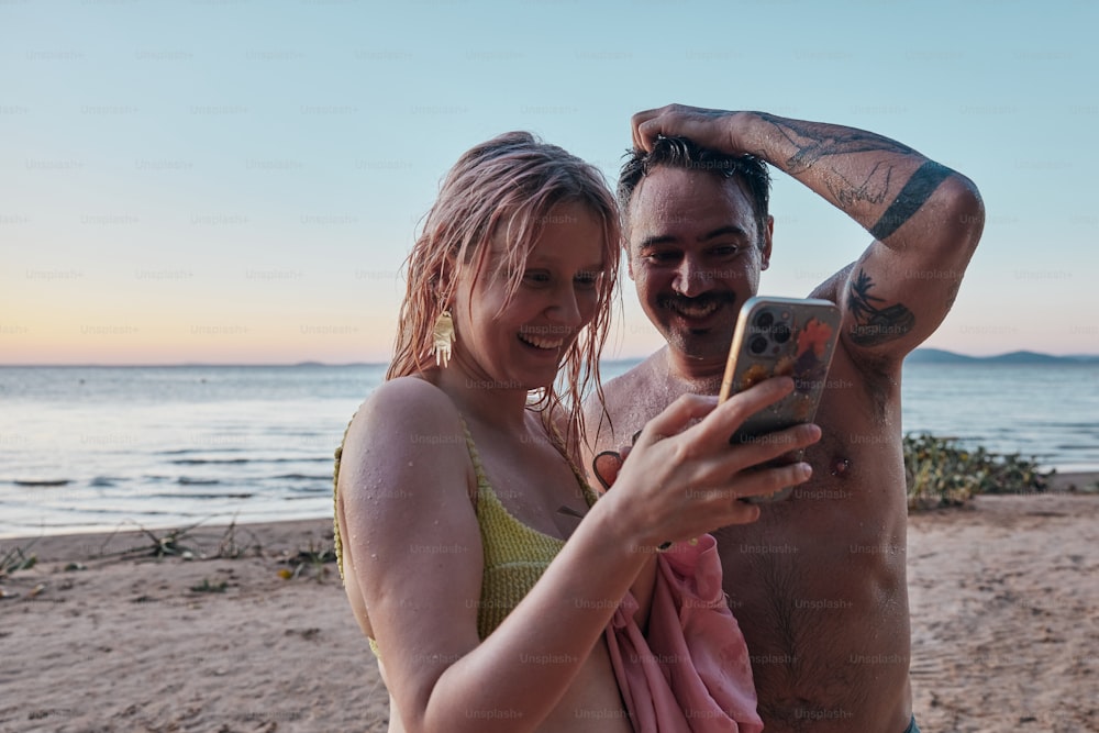 a man and woman standing on a beach looking at a cell phone