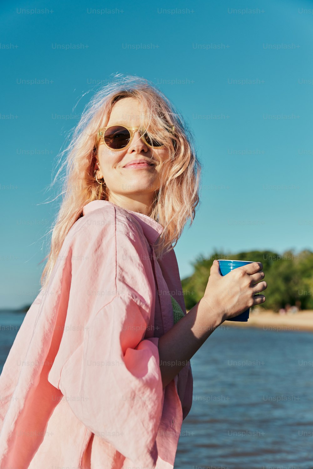 분홍색 셔츠와 선글라스를 쓴 여자가 커피 한 잔을 들고 있다