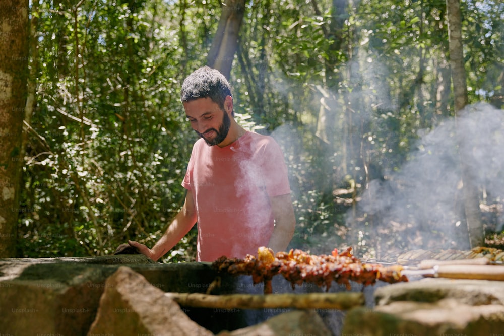 a man cooking on a grill in the woods