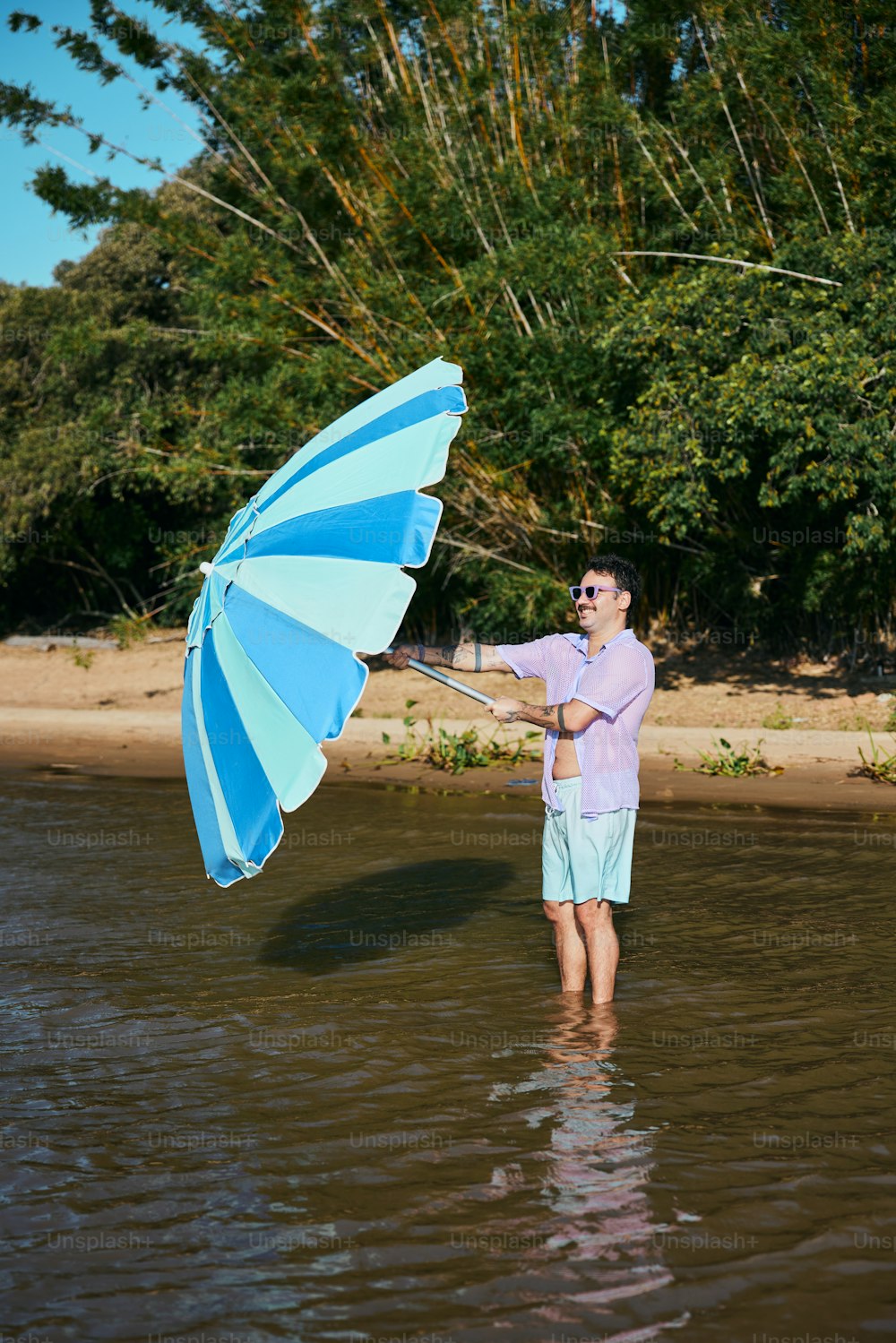 Un uomo in piedi nell'acqua con in mano un ombrello blu e bianco