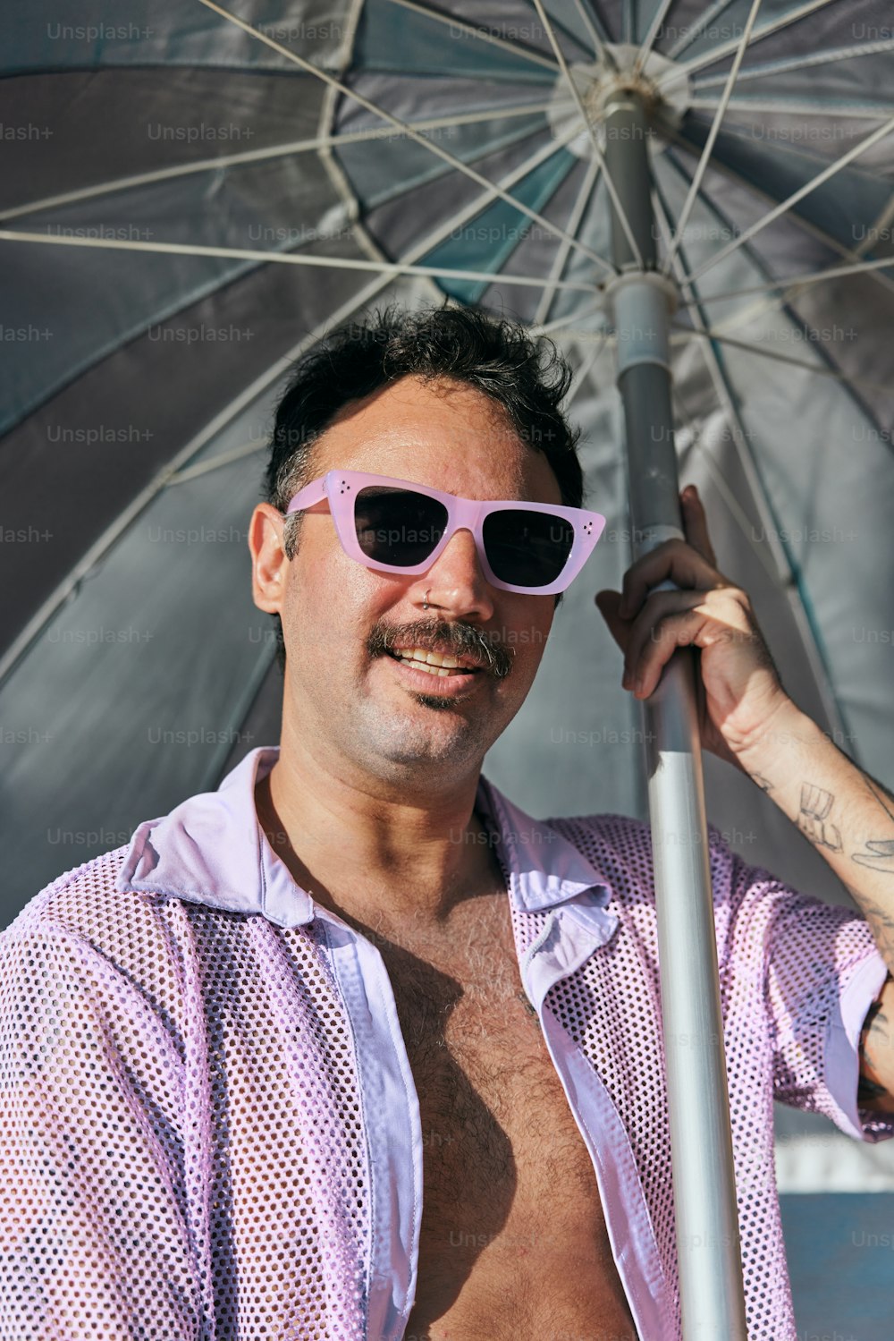 a man in a pink shirt and sunglasses holding an umbrella