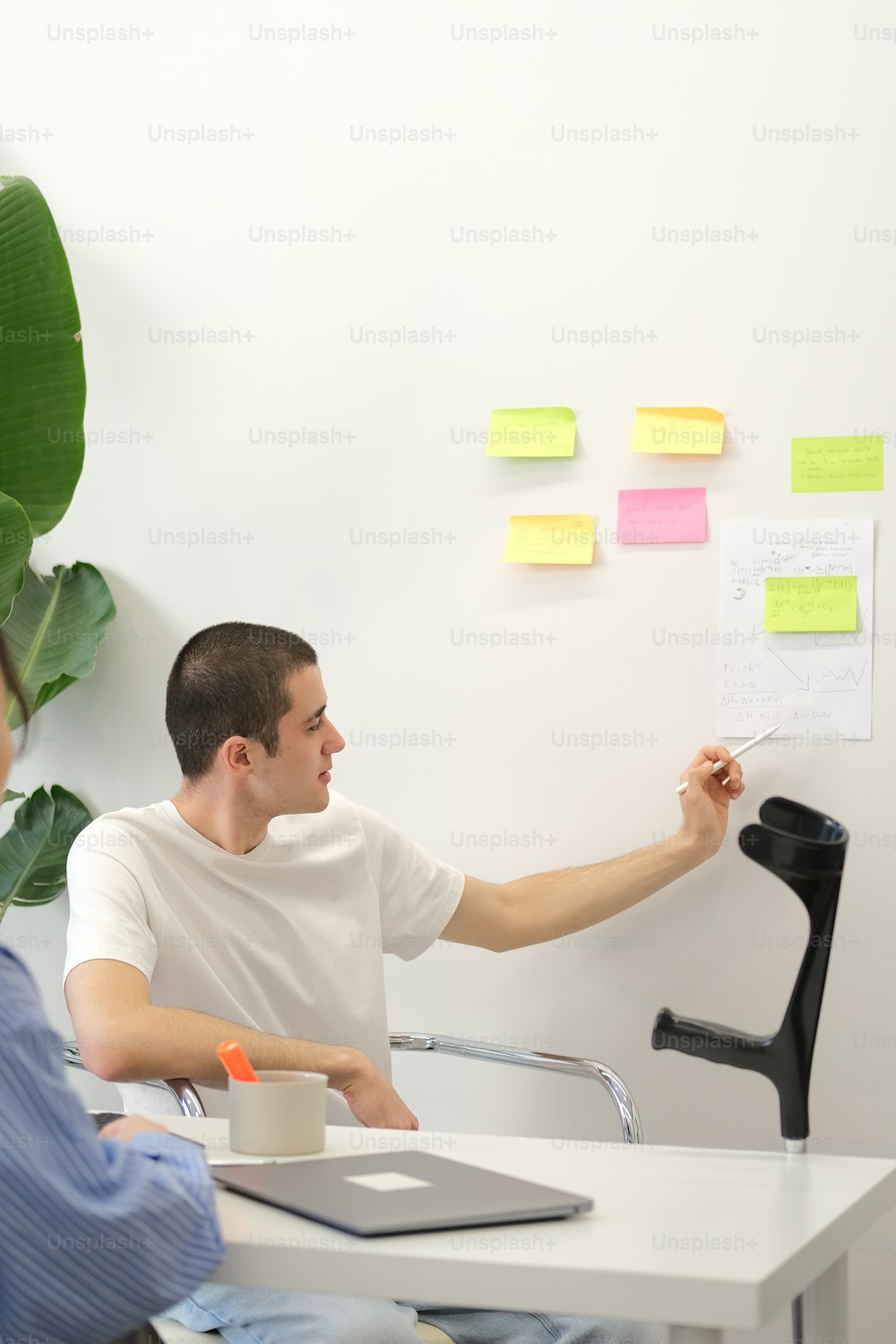a man and a woman sitting at a desk with sticky notes on the wall