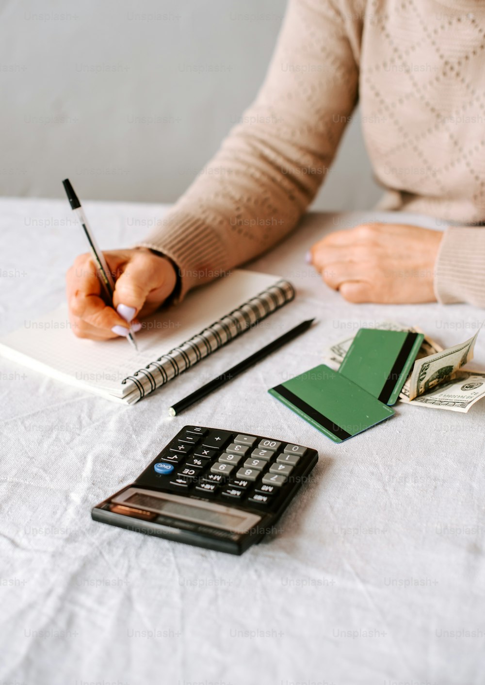 a woman writing on a notepad next to a calculator and money