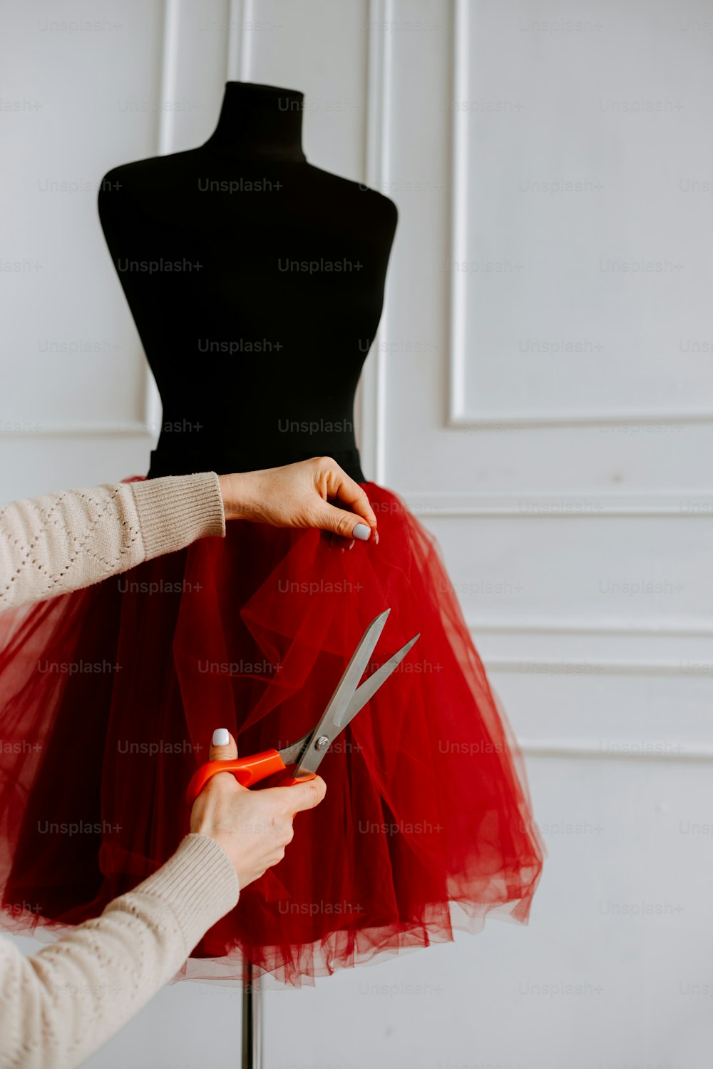 a woman cutting a red tulle with a pair of scissors