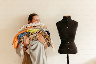 a woman holding a pile of clothes next to a mannequin