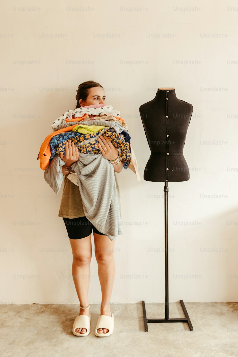 uma mulher segurando uma pilha de roupas ao lado de um manequim