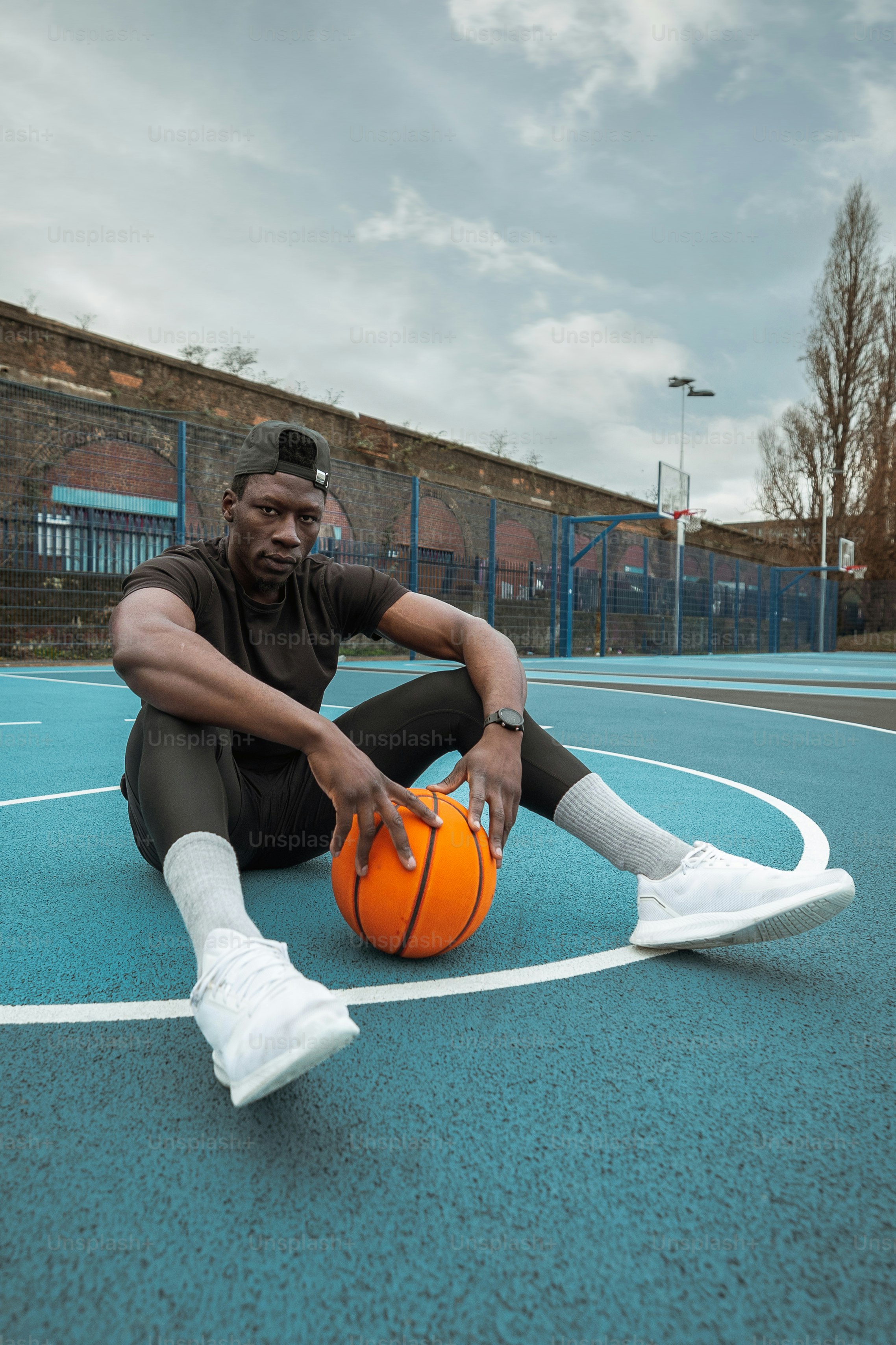 Un hombre sentado en una cancha de baloncesto sosteniendo una pelota de baloncesto