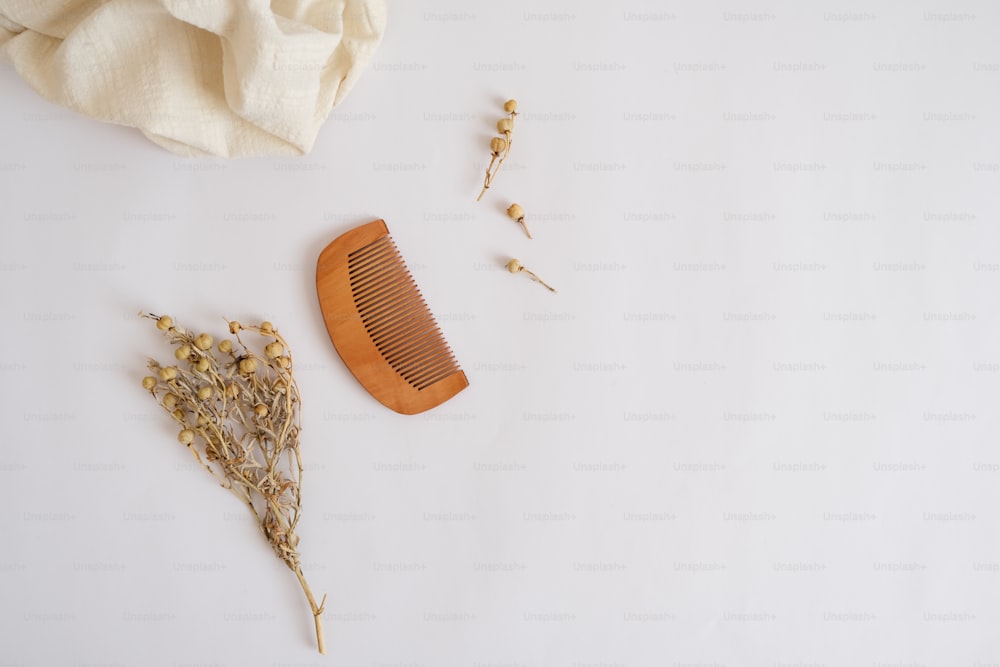 a wooden comb next to dried flowers on a white surface