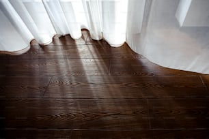 um piso de madeira com uma cortina branca e uma janela