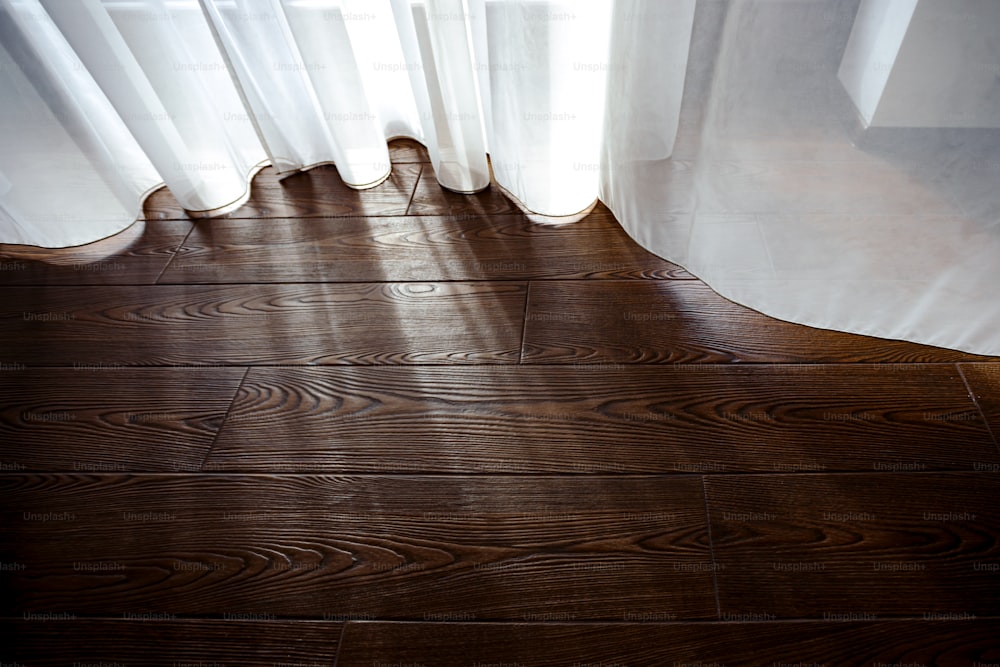 a wooden floor with a white curtain and a window
