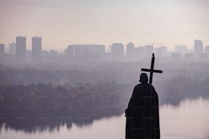 a statue of a person holding a cross in front of a lake