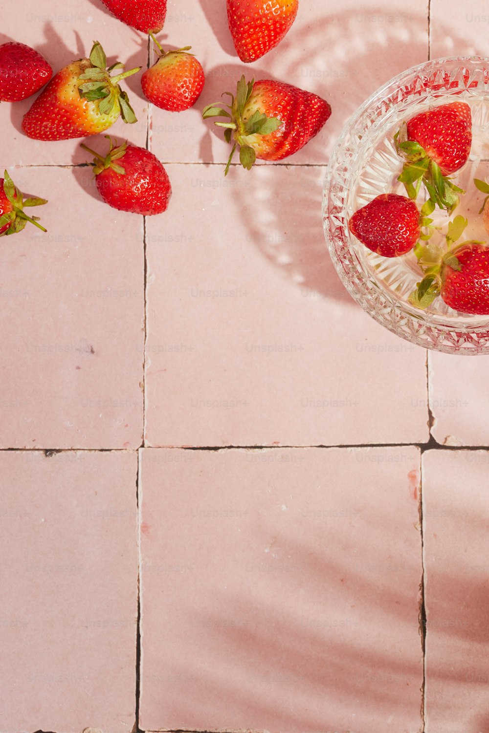 a bowl of strawberries on a pink tile floor