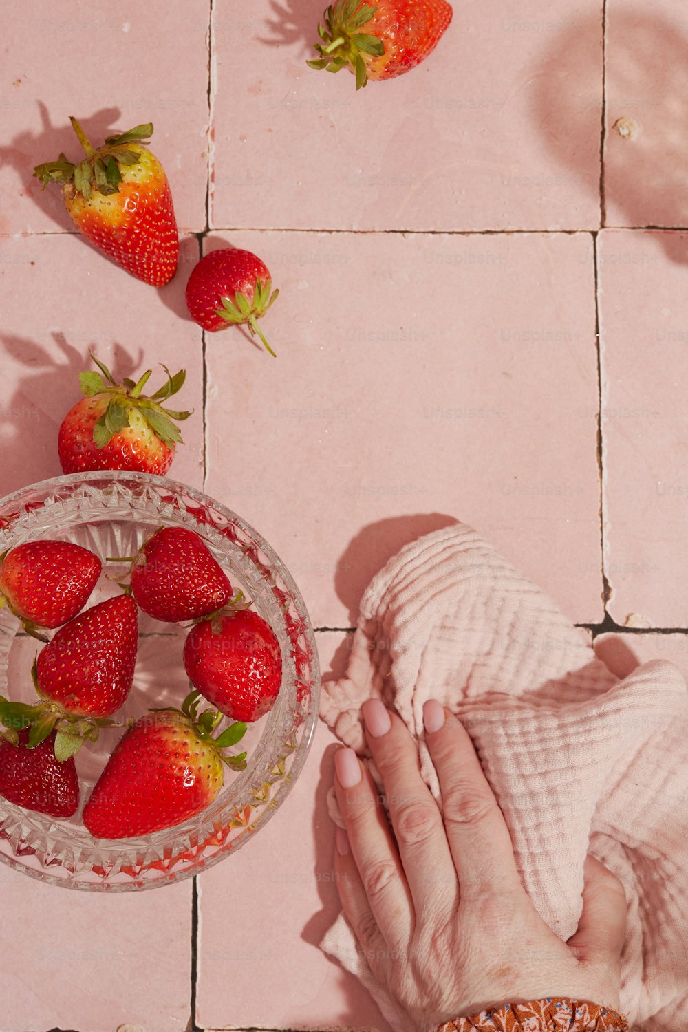 un tazón de fresas y un tazón de fresas en un piso de baldosas rosadas