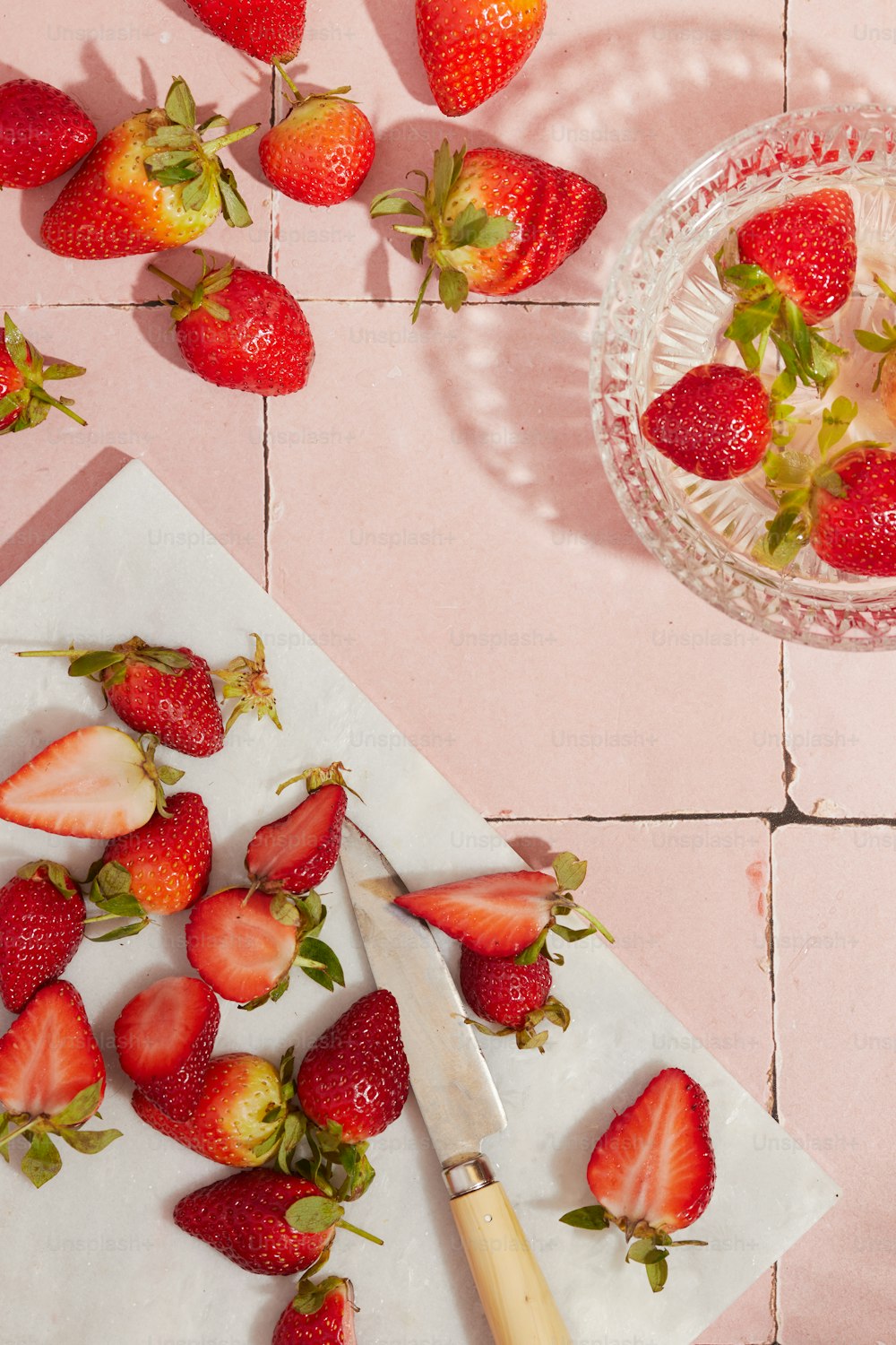 una tabla de cortar cubierta con fresas en rodajas junto a un tazón de fresas