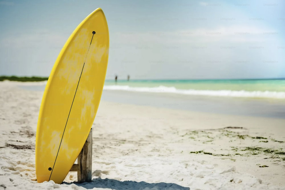 une planche de surf jaune posée au sommet d’une plage de sable