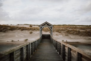 Ein Holzsteg, der zu einem Strand mit Sanddünen im Hintergrund führt