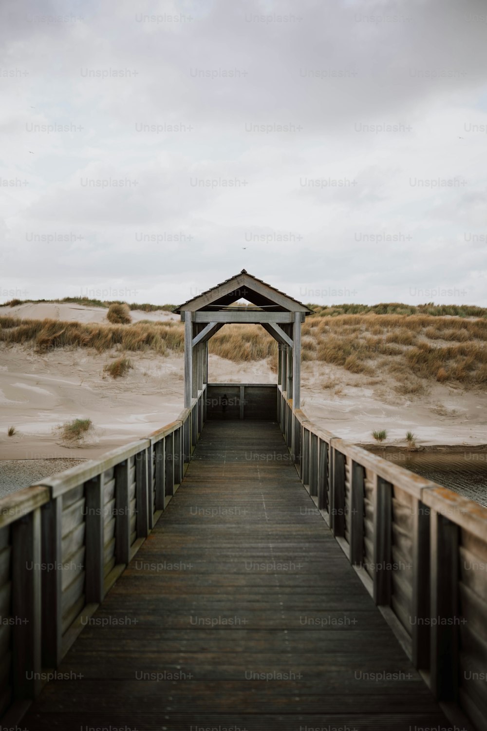 a wooden walkway leading to a beach with sand dunes in the background