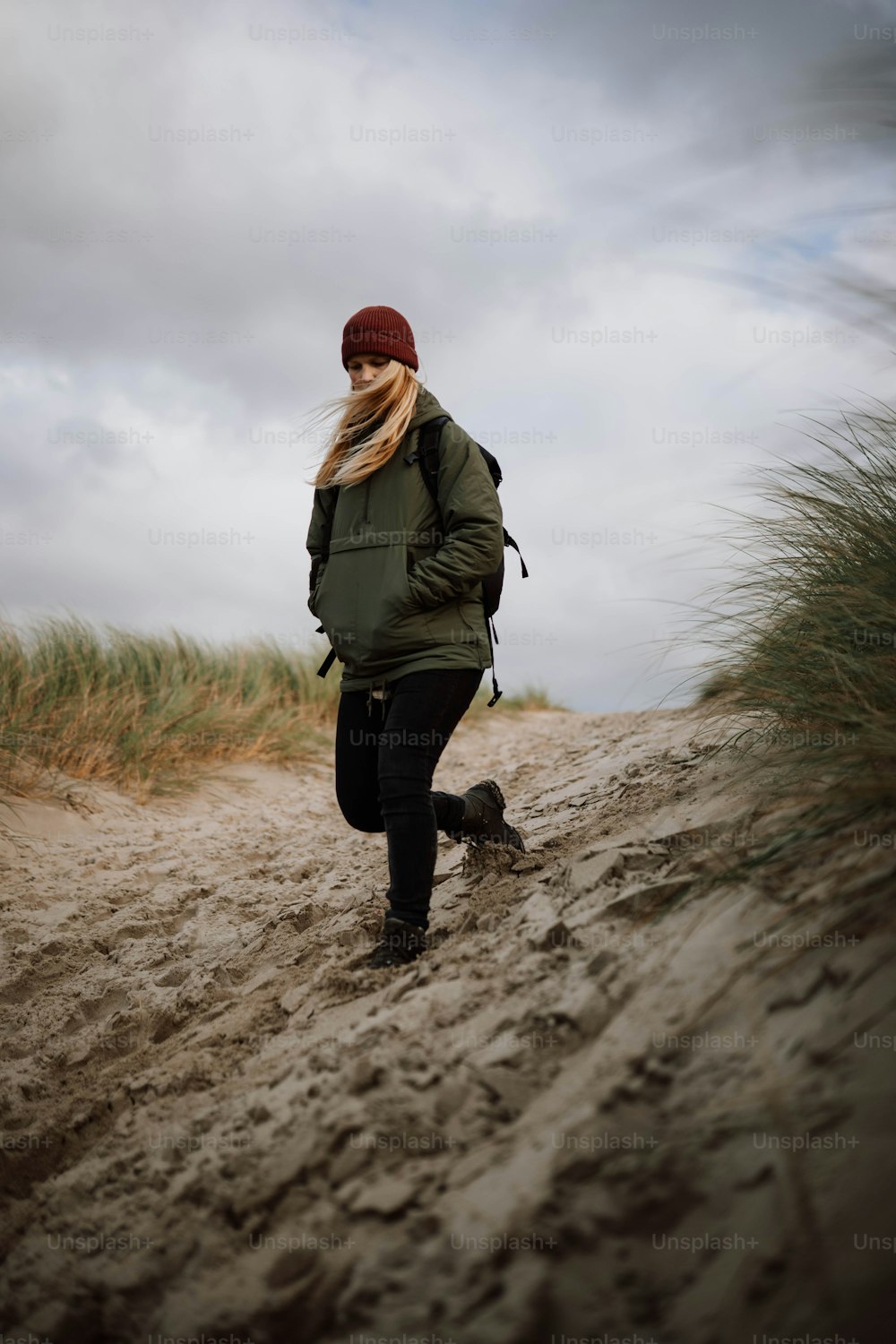 a woman walking down a dirt road next to tall grass