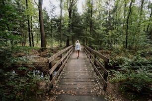 a woman walking across a wooden bridge in a forest