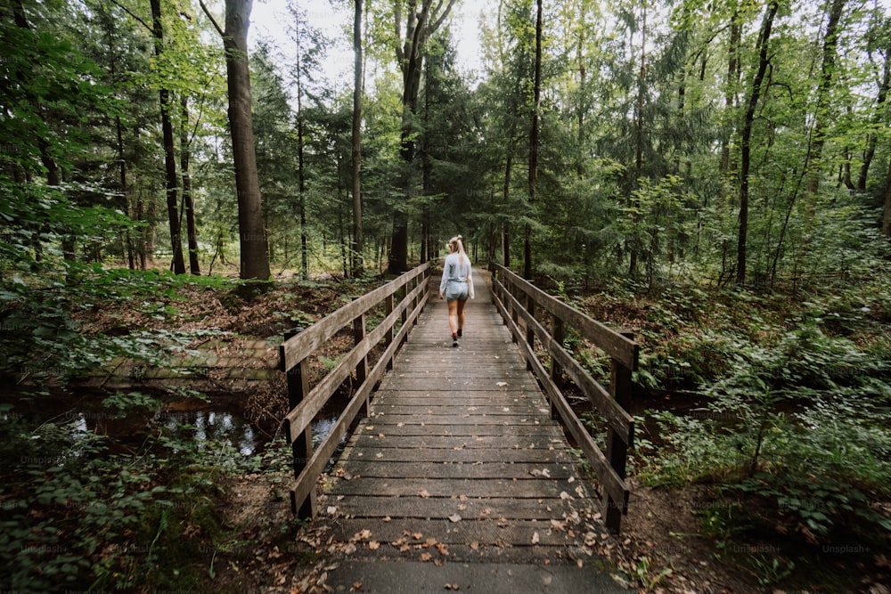 a woman walking across a wooden bridge in a forest