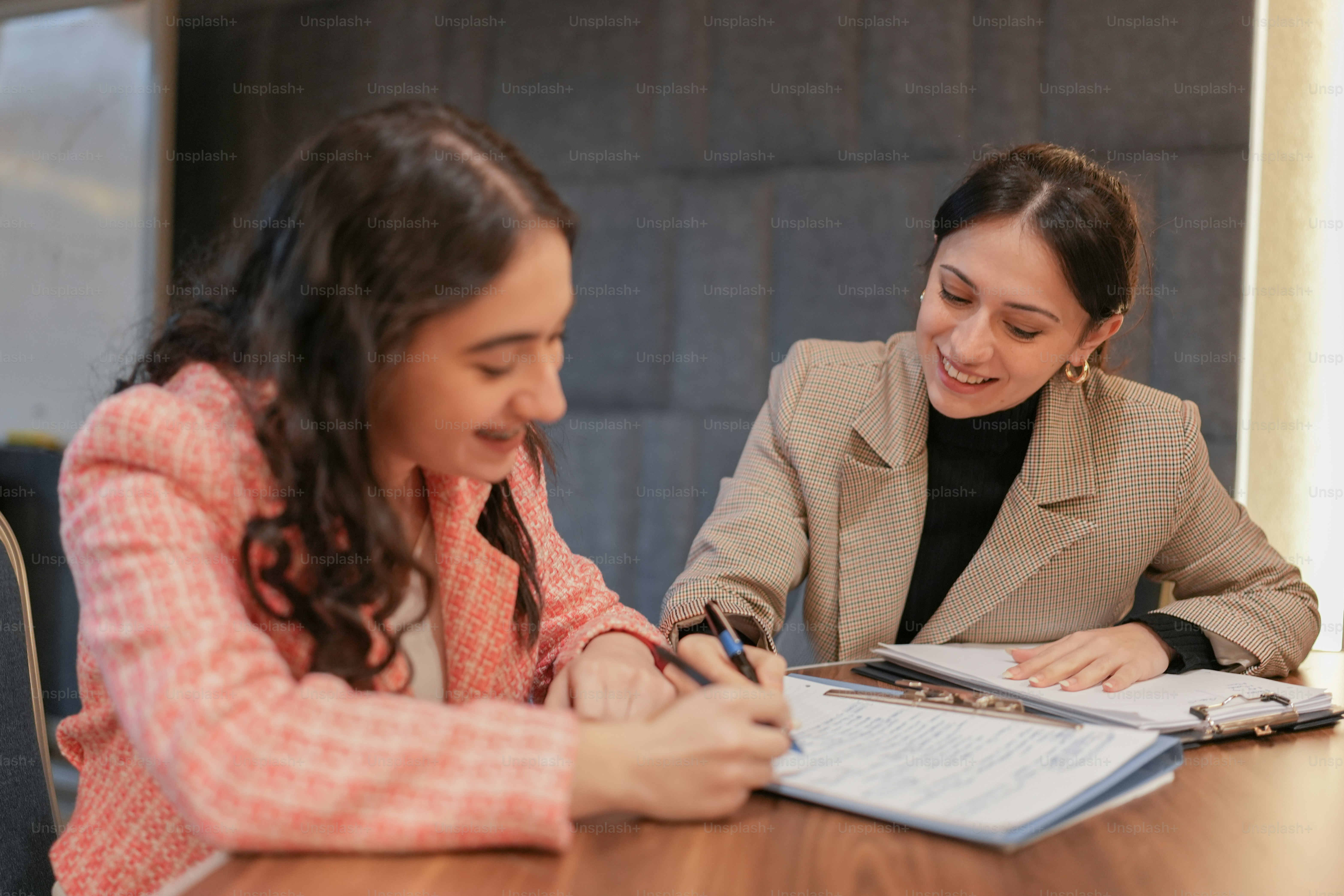 two women sitting at a table with a notebook and pen