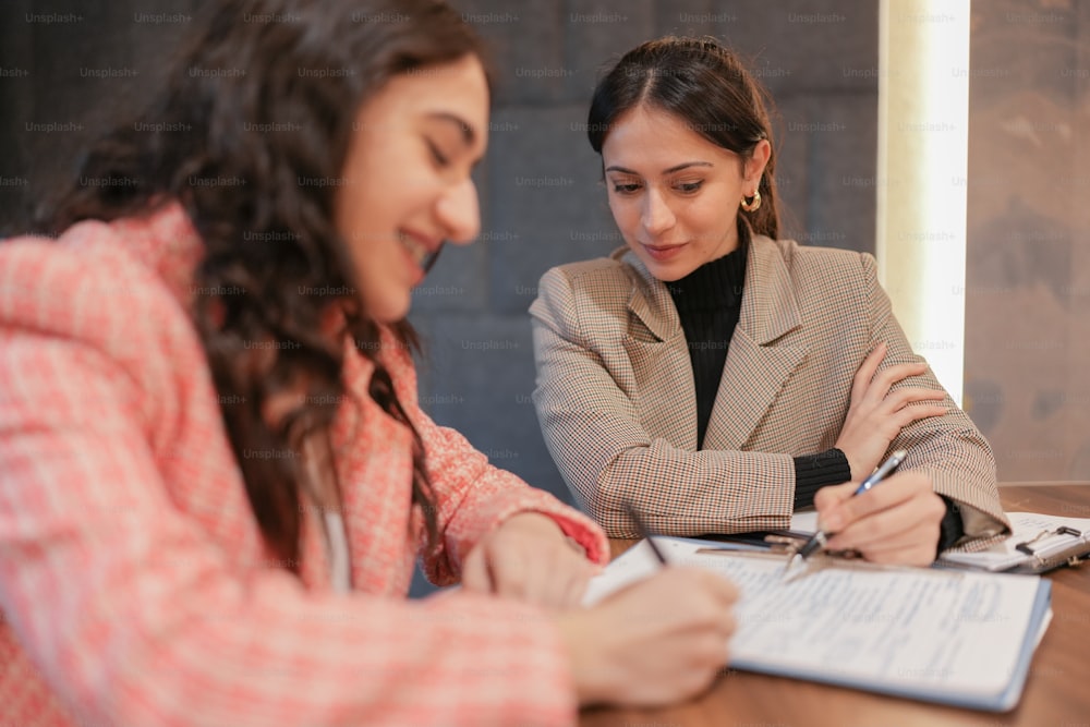 two women sitting at a table signing papers