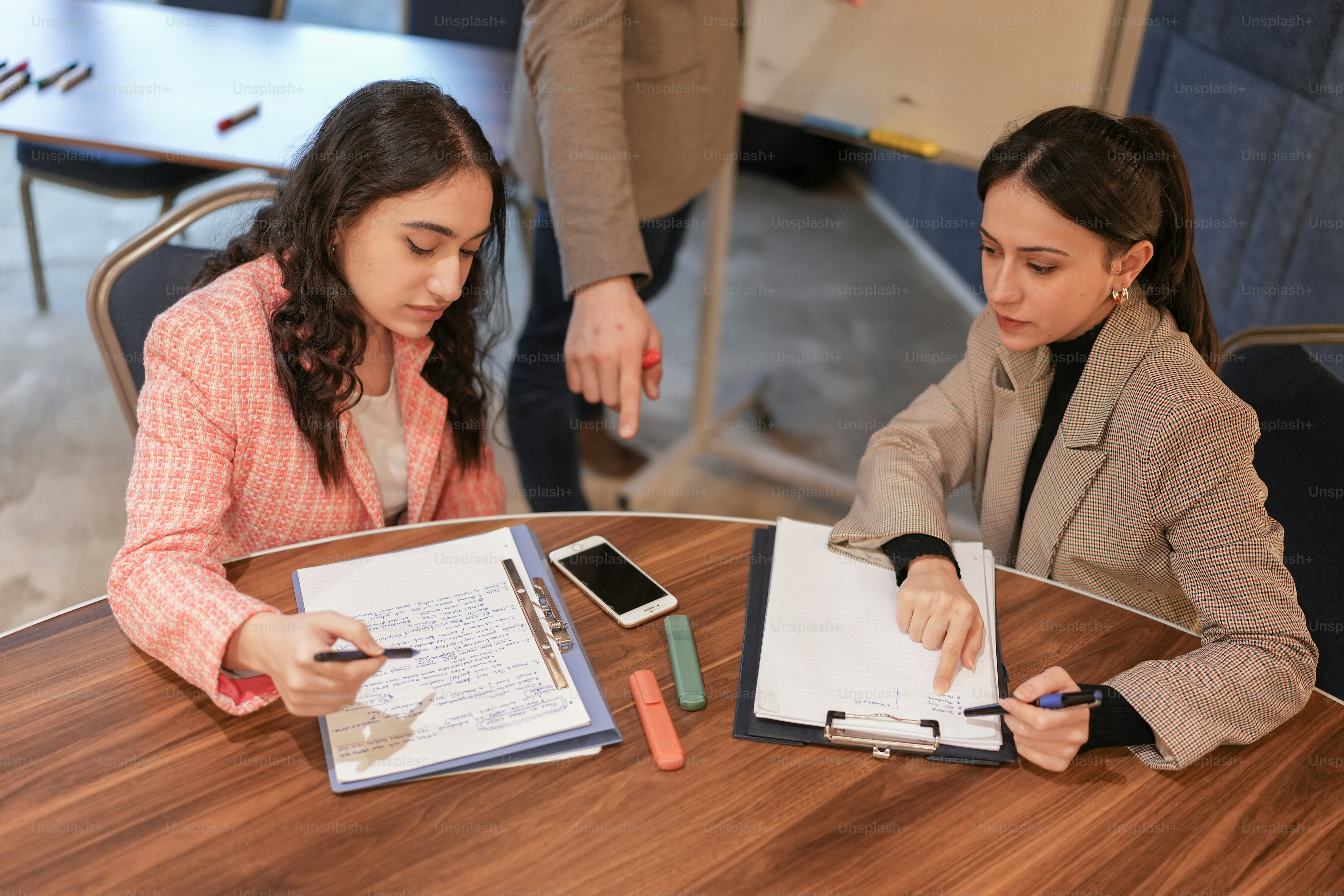 Dos mujeres sentadas en una mesa con cuadernos y teléfonos celulares