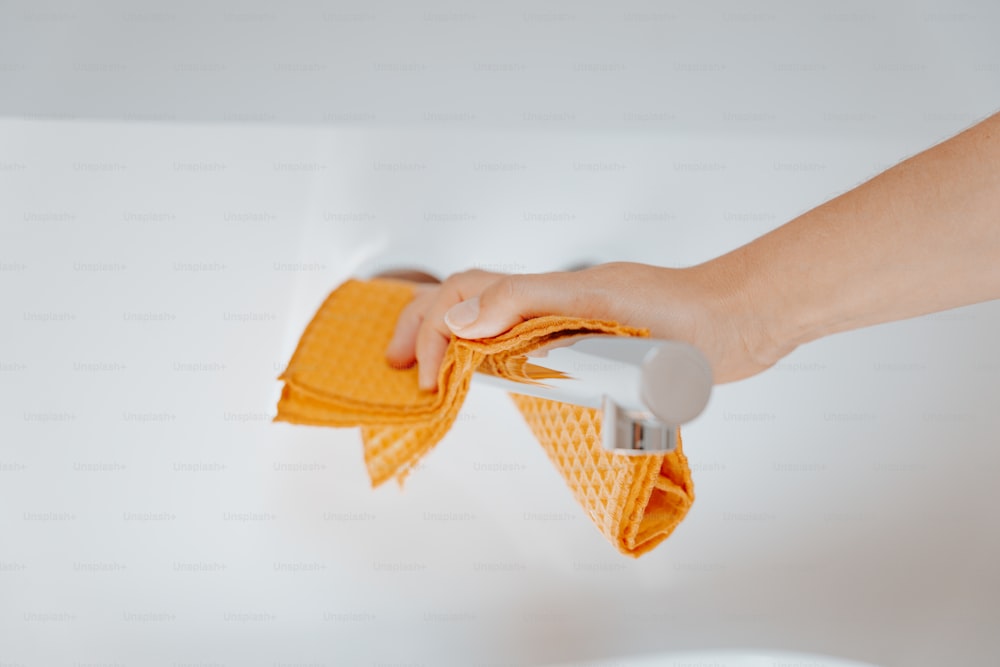 uma pessoa está limpando uma superfície branca com uma toalha amarela